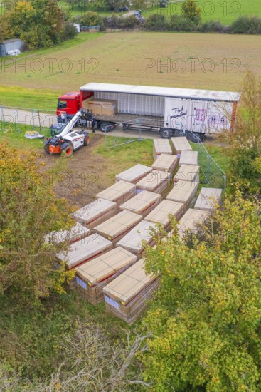 Aerial view of a forklift truck working next to a truck with boxes and autumn trees, PV