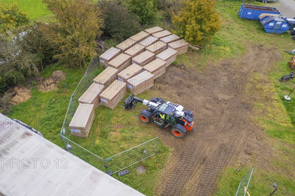 Aerial view of boxes and a forklift truck on a fenced grassy area with containers, PV