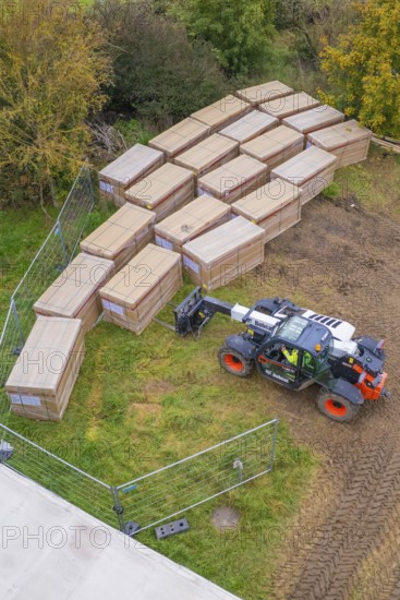 A forklift truck arranges stacked boxes on a fenced meadow in autumn, Bau PV Freifaechenanlage,
