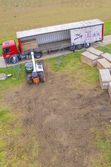 A forklift unloads boxes from a truck in a field next to a road, Bau PV Freifaechenanlage, Weil der
