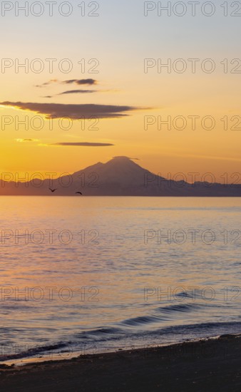 View of Cook Inlet on white mountain peaks of Mount Redoubt at sunset, picturesque golden light of