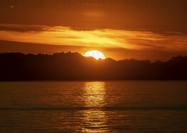 Sun sets behind mountain peaks, view of Cook Inlet at sunset, picturesque golden light of the