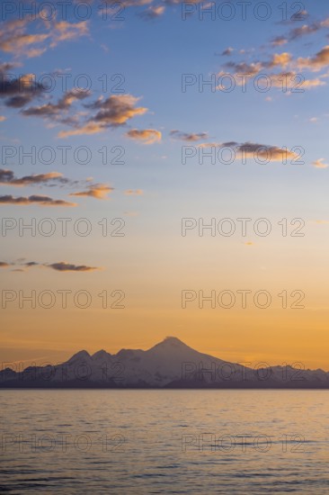 View of Cook Inlet on white mountain peaks of Mount Iliamna at sunset, picturesque golden light of