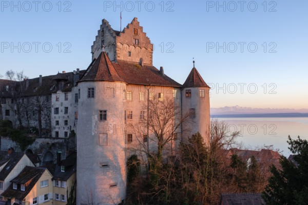 The historic Meersburg Castle, illuminated by the setting sun, right behind it Lake Constance with