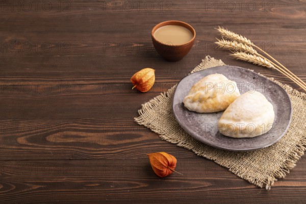 Glazed Pies with Cowberry jam on brown wooden background and linen textile, cup of coffee, side