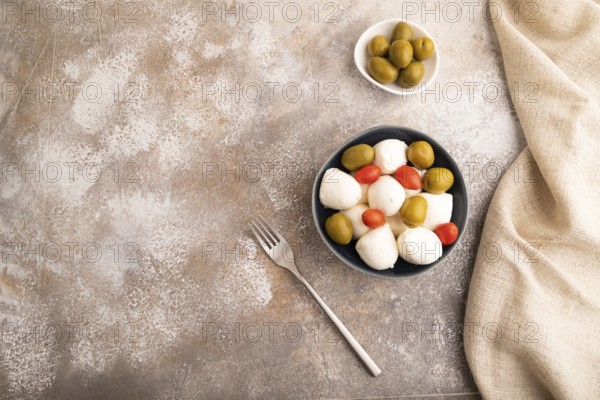 White Mozzarella cheese, with tomatoes and olives in blue bowl on brown concrete background and