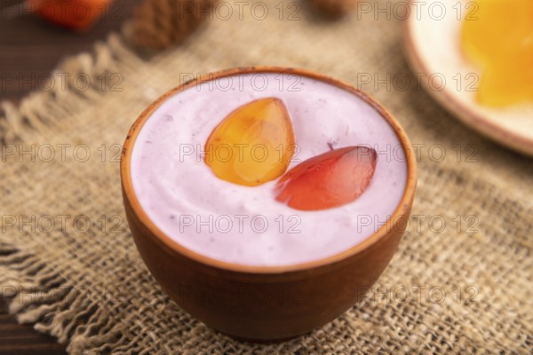 Purple Yogurt, with jelly candy on brown wooden background and linen textile, side view, close up,