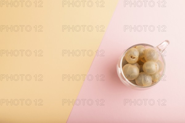 Ripe peeled Longan in glass on pink and orange pastel paper background, top view, flat lay, copy
