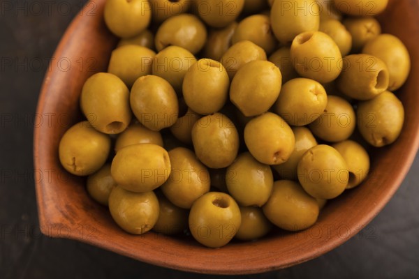 Fresh green olives in ceramic clay bowl on black concrete background. top view, close up, selective