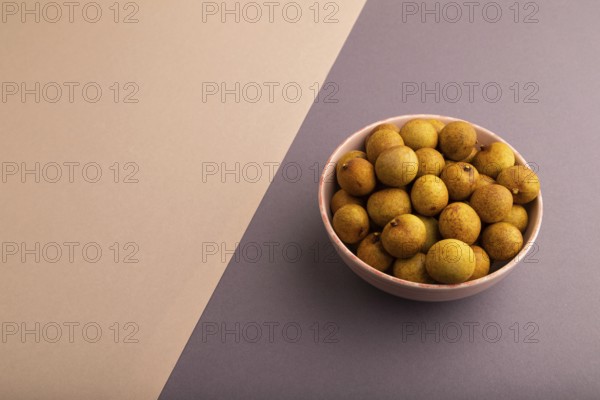 Ripe Longan in ceramic bowl on brown and gray pastel paper background, side view, copy space,
