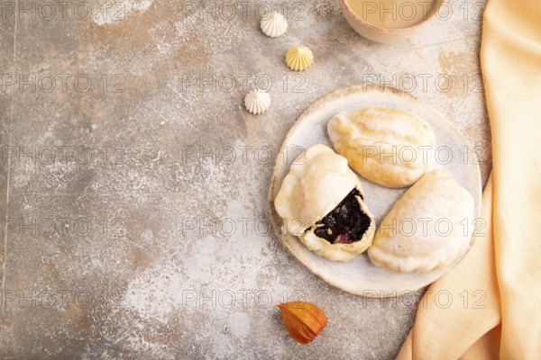 Glazed Pies with blueberry jam on brown concrete background and orange linen textile, cup of