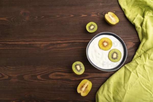 Yogurt, with kiwi in blue bowl on brown wooden background and green linen textile, top view, flat