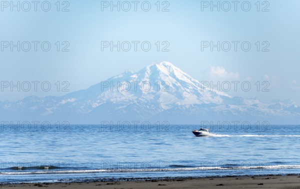 View over Cook Inlet to white mountain peaks of Mount Redoubt, motor boat rides on the ocean,