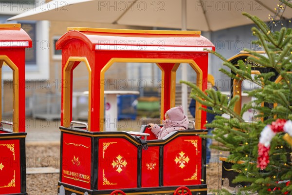 A child sits on a red miniature train next to a Christmas tree at a market, Sindelfingen, Böblingen