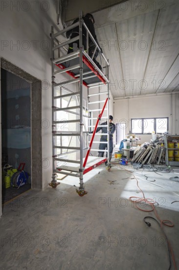High scaffolding in an unfinished interior with a worker, construction in progress, electrician,
