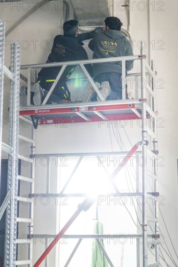 Two workers standing on scaffolding and working on a ceiling with strong light, electrician, new