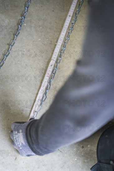 A hand pulls on a chain lying on the ground next to a tape measure, electrician, new building,