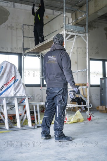 A worker on scaffolding works in a construction site, another worker standing next door,