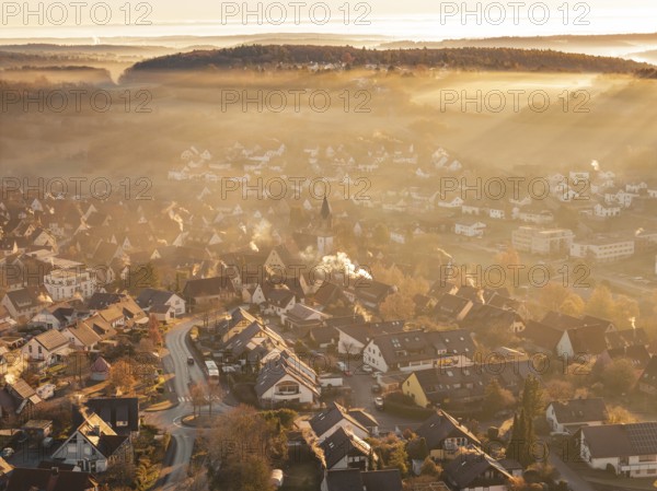 Fog-covered village with church tower in morning light with surrounding hills and mountains,