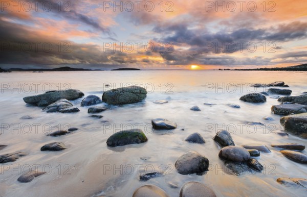 Orange cloudy sky at sunset on a sandy beach with round stones near Achiltibuie on the west coast