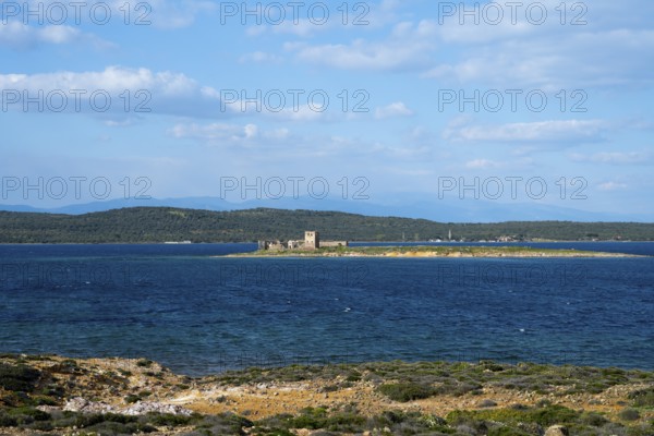 A small island with ruins is surrounded by a deep blue sea under clear skies, ruins of Agios Yorgis