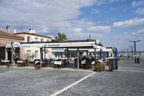 Seaside restaurant with outdoor seating area under blue and white skies, relaxed atmosphere and