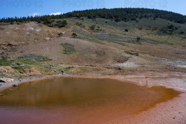 Small red lake in a geological mountain landscape under blue sky, geothermal area, rainbow rocks