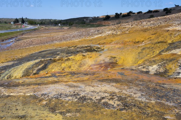 A colorful natural landscape with yellow and orange rocks next to a road under a blue sky,