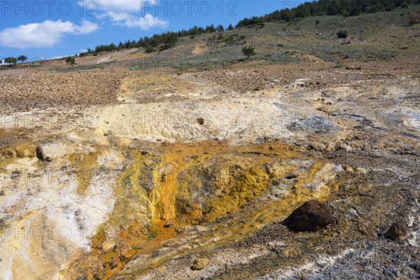 Geological landscape with hills and earthy tones under a partly cloudy blue sky, geothermal area,
