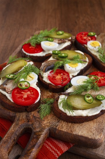 Sandwiches on rye bread with sprats, quail eggs, fresh tomatoes and pickled cucumber, on a wooden
