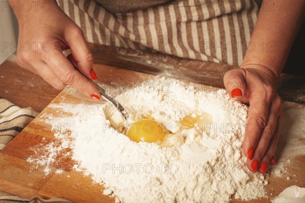 A person with bright nails is combining eggs with flour on a wooden board. The setting is a cozy
