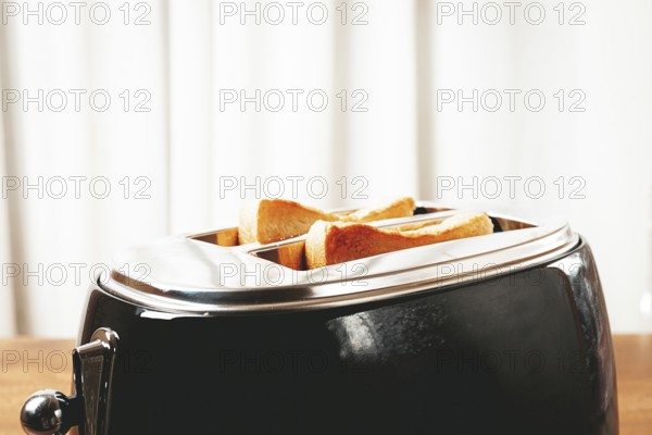 Two slices of bread are toasting in a shiny metal toaster, set on a countertop in a warm kitchen.