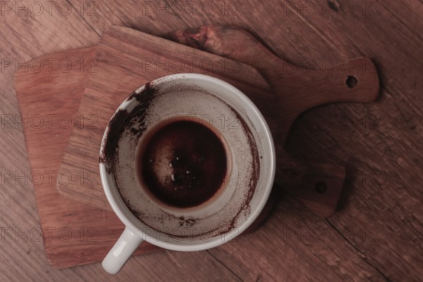 A warm coffee cup sits on a wooden cutting board, showing traces of dark liquid and coffee grounds.