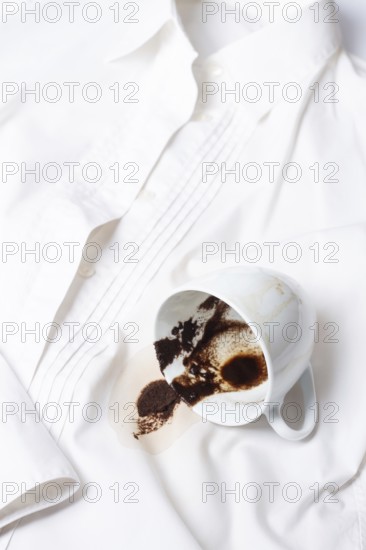 A white cup with the remains of coffee, spilled, lies on a white shirt, there are no people, a soft