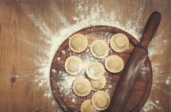 Fresh raw, uncooked ravioli, on a cutting board, with a rolling pin for dough, wooden background,