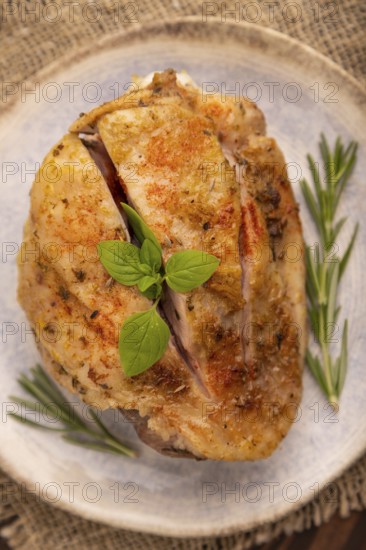 Fried Turkey Thigh with spices and rosemary on plate on brown wooden background and linen textile.