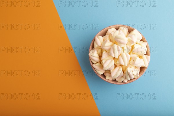 Orange and pink marshmallow in ceramic bowl on blue and orange pastel paper background, top view,