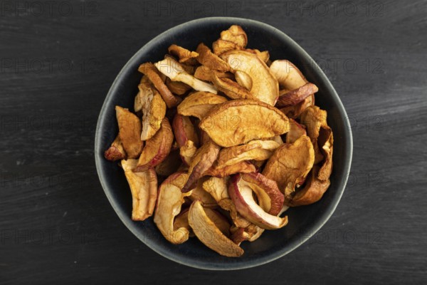 Dried Apples in ceramic bowl on black wooden background. Top view, close up, flat lay. healthy