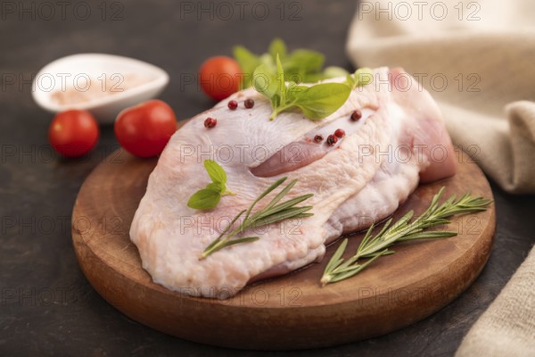 Raw Turkey Thigh with spices and rosemary on cutting board on black concrete background and linen