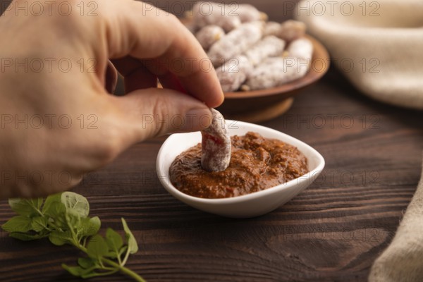 Small smoked Chicken sausages in wooden bowl with hand on brown wooden background and linen textile