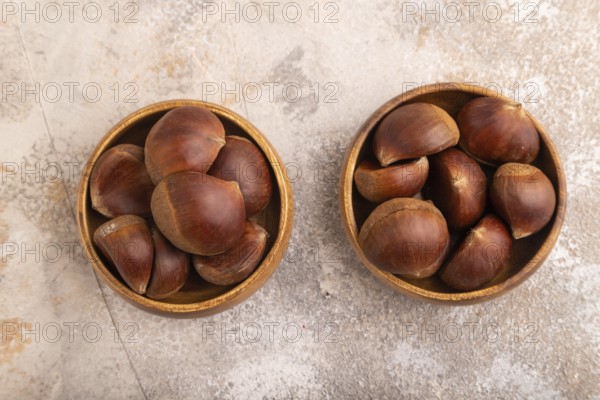 Wooden bowl with raw edible Ð¡hestnuts on brown concrete background, top view, flat lay, close up,