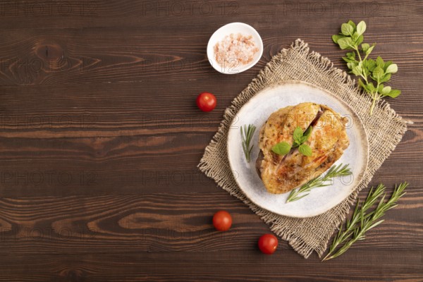Fried Turkey Thigh with spices and rosemary on plate on brown wooden background and linen textile.