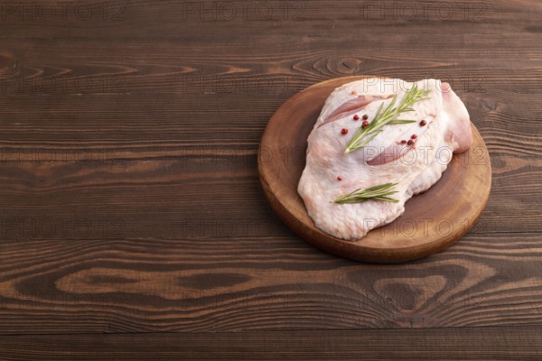 Raw Turkey Thigh with spices and rosemary on cutting board on brown wooden background. side view,