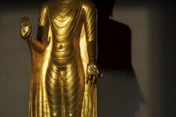 Standing gilded Buddha statue, the right hand (raised, open palm facing outwards) symbolises the