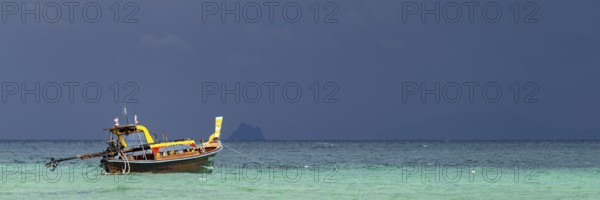 Longtail boat (Thai: Ruea Hang Yao) on the beach, behind it an approaching thunderstorm, Koh Ngai