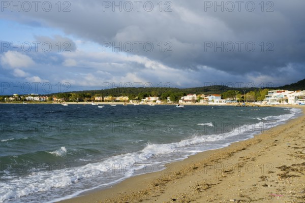 A beach with soft waves, cloudy skies and houses along the coast, beach near GÃ¼zelyali,
