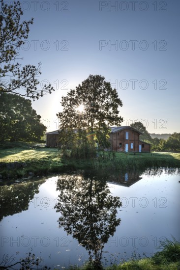 Manor with historic stable and pond, from 1923, in backlight with sun star, Gut Othenstorf,