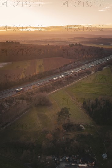 Aerial view of a motorway surrounded by fields and forests as the orange sunset colors the sky, A8