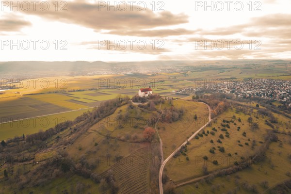 A hill with a church and a wide view over fields and a village under a cloudy sky, Wurmlinger