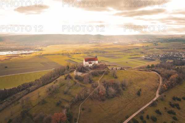 Panoramic view of a church on a hill with surrounding fields and vast clouds, Wurmlinger Chapel,